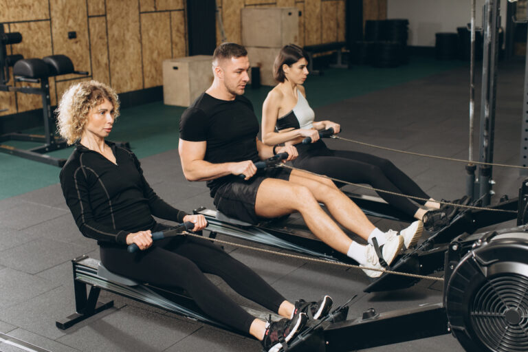 Young man and beautiful women working out with rowing machine at crossfit gym.